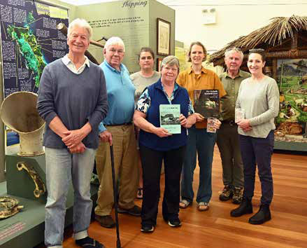 A group of people, two holding books, in Lord Howe Island Museum backed by a shipwreck display