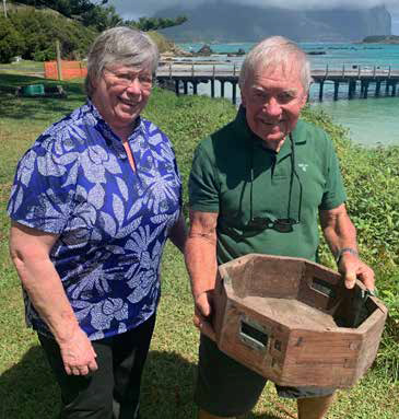 A man and a woman standing near a wooden jetty holding an old wooden compass box