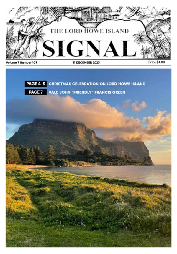 On the front page of the December edition of the Lord Howe Island Signal, is a gorgeous beach scene. In the foreground, there is a lush green shoreline. In the background, a tall mountain sits under soft clouds.