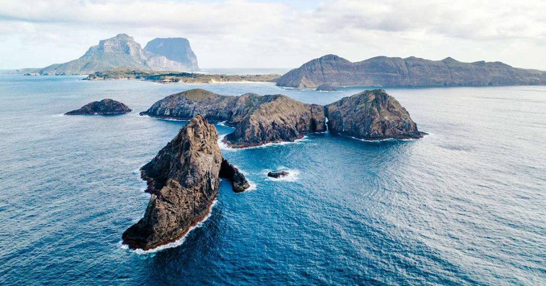 This image is a beautiful aerial shot looking across the blue ocean over the Admiralty Islands in the foreground and Lord Howe Island in the background.