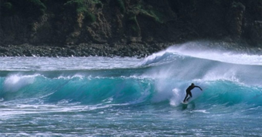 This image is of a surfer catching a beautiful blue wave.