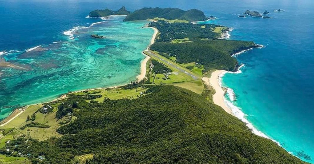 This aerial image captures the stunning Lord Howe Island, featuring the Airstrip in the middle of the Island. The Island's lush greenery, pristine beaches, and crystal-clear waters create a picturesque and serene environment.