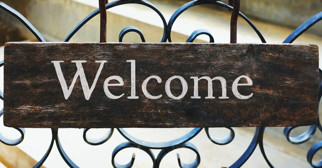 A sign that says welcome hanging on a iron fence.